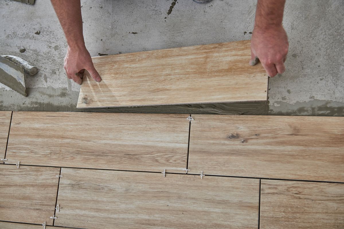 Laying wood effect tiles on the floor. Worker laying floor tiles.